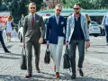 Trois hommes élégants déambulent. L'un porte une tenue avec blazer bleu ciel, un autre un costume vert olive, et le troisième un blazer gris clair.