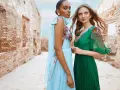 Deux femmes portent des robes élégantes, parfaites pour une tenue mariage avril. L'une est en bleu ciel plissé, l'autre en vert émeraude.