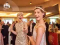 Deux femmes dansent, l'une porte une robe à paillettes dorées et un bandeau, l'autre une robe à franges, parfaites pour une tenue guinguette femme.