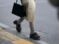 Une femme marche dans la rue, portant un sac noir et un élégant sabot femme marron clouté avec des chaussettes grises.