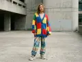 Jeune femme portant un gilet coloré style oversize et un pantalon tie-dye, devant un bâtiment en béton.