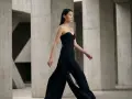 Mannequin portant une combinaison noire bustier, avec des jambes évasées. Quelles chaussures avec une combinaison noire ? Des talons fins pour allonger la silhouette.