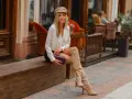 Une femme élégante assise dehors, portant une tenue chic avec des bottes hautes beiges. Idée de comment porter des bottes hautes marrons avec style.