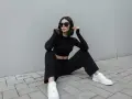Une femme en tenue noire, crop top et pantalon large, assise sur des pavés. Idée de comment porter un pantalon large avec des baskets blanches.