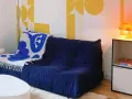 Canapé bleu profond avec plaid blanc et bleu, sur fond de papier peint jaune géométrique en **color blocking**. Lampe orange sur une étagère.