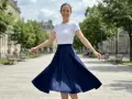 Une femme en talon et jupe évasée bleue danse joyeusement dans une rue parisienne bordée d'arbres.