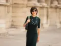 Une femme élégante porte une robe midi vert foncé, un collier de perles et des lunettes de soleil. La robe midi définition est une longueur polyvalente.