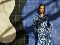 Une femme pose devant un mur de carreaux bleus et blancs. Sa robe à motifs bleus et blancs s'harmonise parfaitement avec le décor. Quelle couleur va bien avec le bleu vêtement ? Le blanc, évidemment !