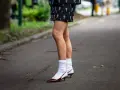 Jambes portant une jupe ornée et des escarpins bordeaux avec une chaussette par dessus chaussure blanche.
