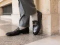 Un homme porte un pantalon gris retroussé et une chaussette mocassin noire avec une boucle dorée.