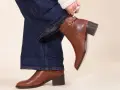 Une femme ajuste sa tenue avec bottines marron. Un jean évasé et un pull blanc complètent le look.