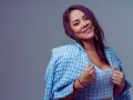 Une femme de 40 ans moderne, souriante, porte une veste à carreaux bleus et blancs sur un haut assorti. Son regard est captivant.