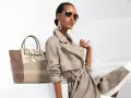 Une femme incarne le **style classique femme** avec un trench léger, des lunettes aviateur et un grand sac bicolore.