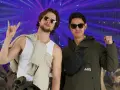 Deux amis profitent d'un concert, l'un fait un signe rock'n'roll, l'autre un poing levé. Leur tenue festival pluie est parfaite pour l'ambiance.