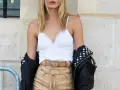 Une femme porte un débardeur blanc en dentelle, un short en cuir beige avec une ceinture assortie, et une veste en cuir noire cloutée.