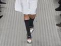 Une mannequin défile avec une tenue blanche et des chaussettes hautes grises, rehaussée par des chaussures argentées pointues.