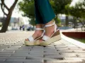 Pieds portant des sandales compensées blanches à plateforme sur un trottoir pavé.