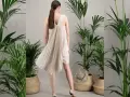 Une femme porte une robe plissée beige, parfaite pour une tenue mariage septembre. Elle est entourée de plantes vertes luxuriantes dans des paniers en osier.