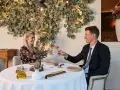 Un couple trinque avec du vin rosé dans un restaurant gastronomique, décoré de feuilles stylisées et d'une lampe design.