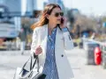 Une femme élégante porte une tenue avec blazer blanc, chemise à rayures bleues et un sac noir, tout en téléphonant.