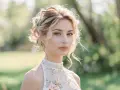 Une jeune femme au chignon flou, portant une tenue mariage religieux femme ornée de fleurs et de perles, pose en extérieur.