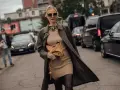 Une femme élégante pose dans la rue, portant une robe courte beige et un long manteau kaki. Elle montre quelle veste porter avec une robe courte pour un look chic.