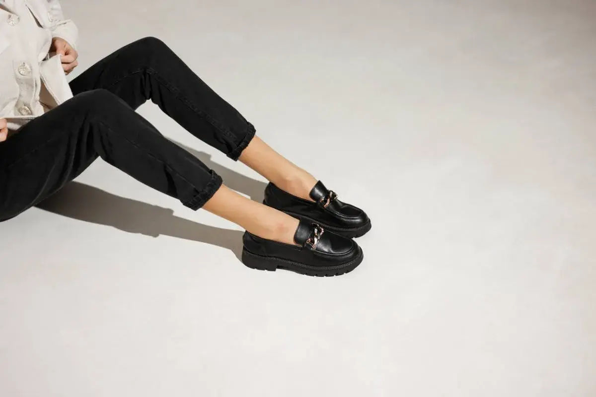 Une tenue décontractée avec un jean noir et une veste claire, rehaussée par une élégante tenue avec mocassin femme orné d'une chaîne dorée.