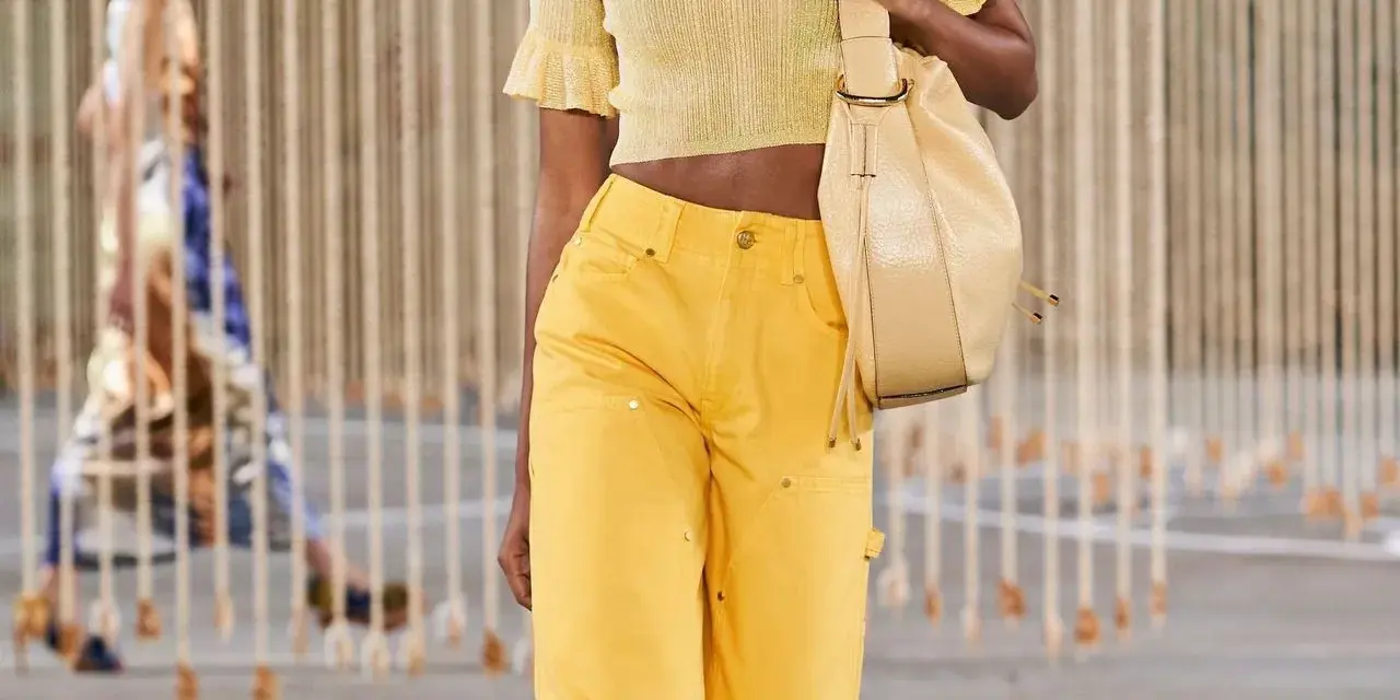 Mannequin portant une tenue de soirée en jean jaune vif, un haut court assorti et un sac beige.