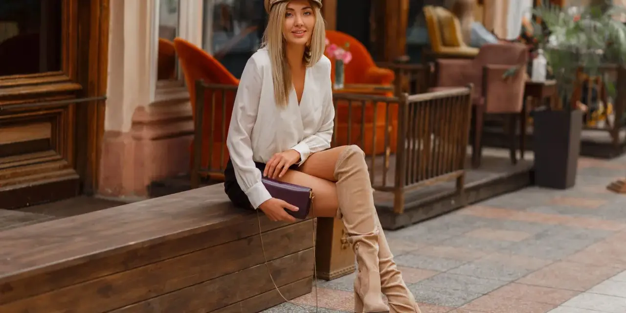 Une femme élégante assise dehors, portant une tenue chic avec des bottes hautes beiges. Idée de comment porter des bottes hautes marrons avec style.