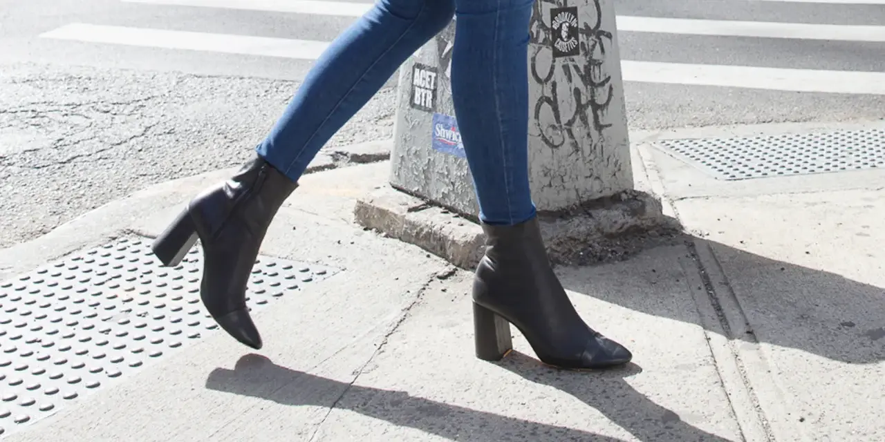 Une femme marche dans la rue avec un jean slim et des bottines noires à talons.