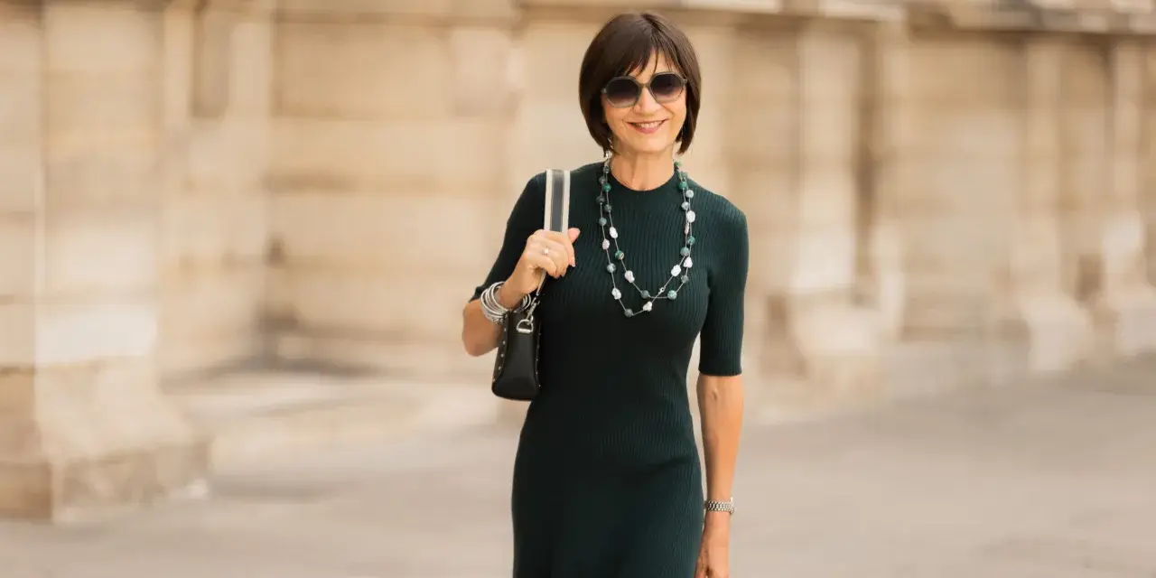 Une femme élégante porte une robe midi vert foncé, un collier de perles et des lunettes de soleil. La robe midi définition est une longueur polyvalente.