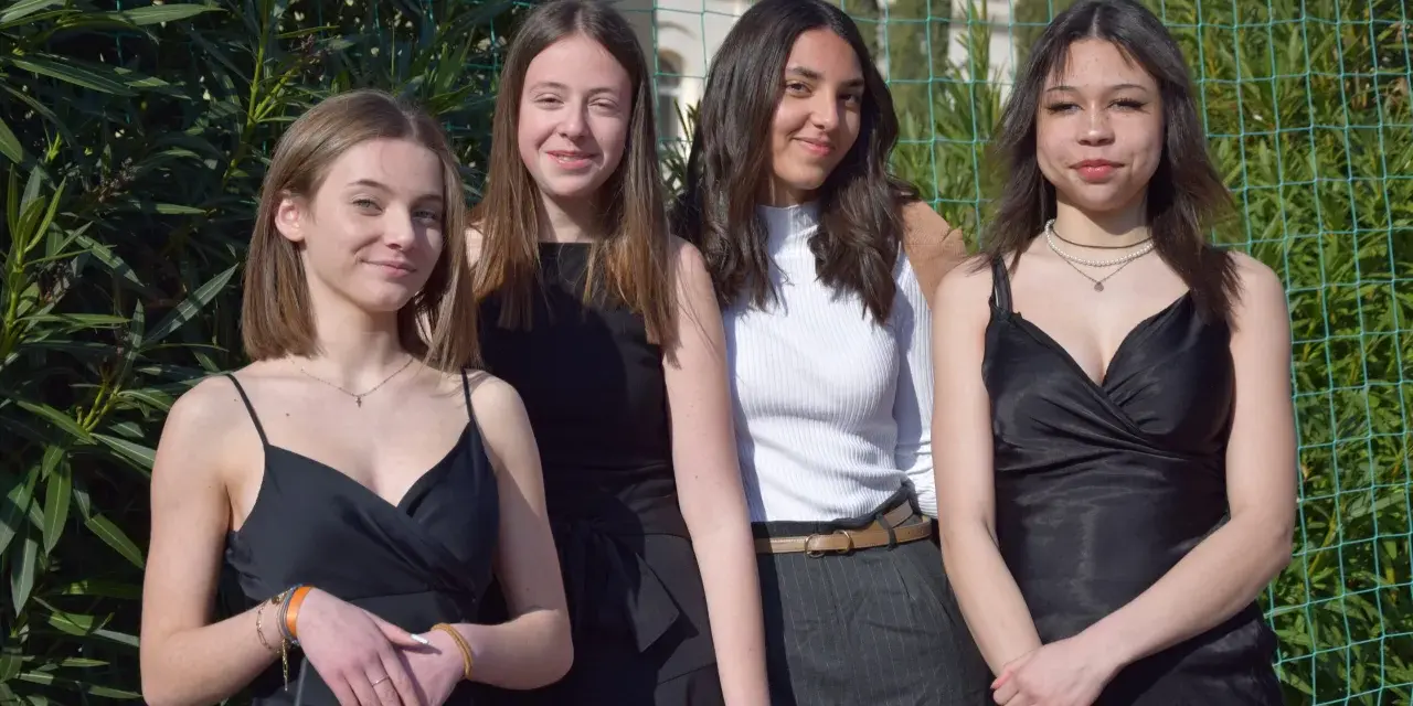 Quatre jeunes femmes posent, habillées élégamment. Idées pour comment s'habiller pour l'Aïd : robes noires, haut blanc chic, et accessoires discrets.