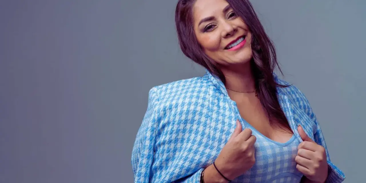 Une femme de 40 ans moderne, souriante, porte une veste à carreaux bleus et blancs sur un haut assorti. Son regard est captivant.
