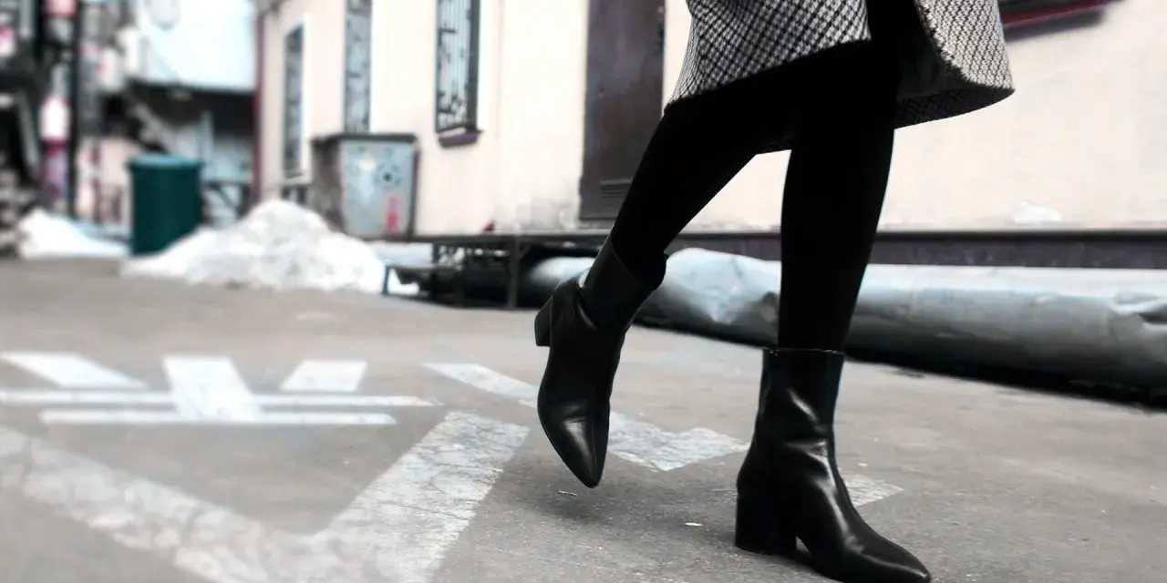 Une femme porte une tenue avec des chelsea boots femme noires, un manteau à carreaux et des collants.