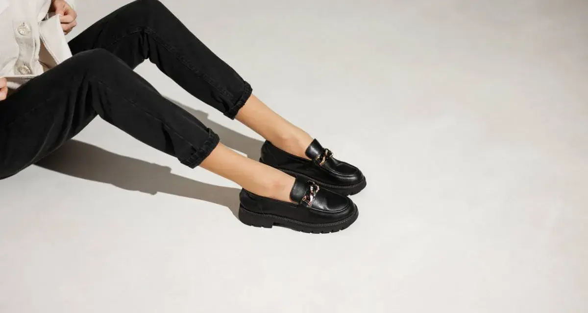 Une tenue décontractée avec un jean noir et une veste claire, rehaussée par une élégante tenue avec mocassin femme orné d'une chaîne dorée.