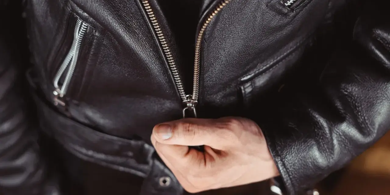 Main d'homme fermant la fermeture éclair d'une veste en cuir noire, partie d'un outfit classique et intemporel.