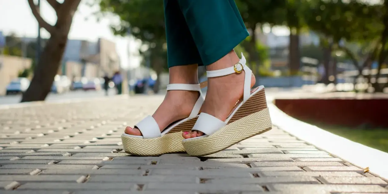 Pieds portant des sandales compensées blanches à plateforme sur un trottoir pavé.