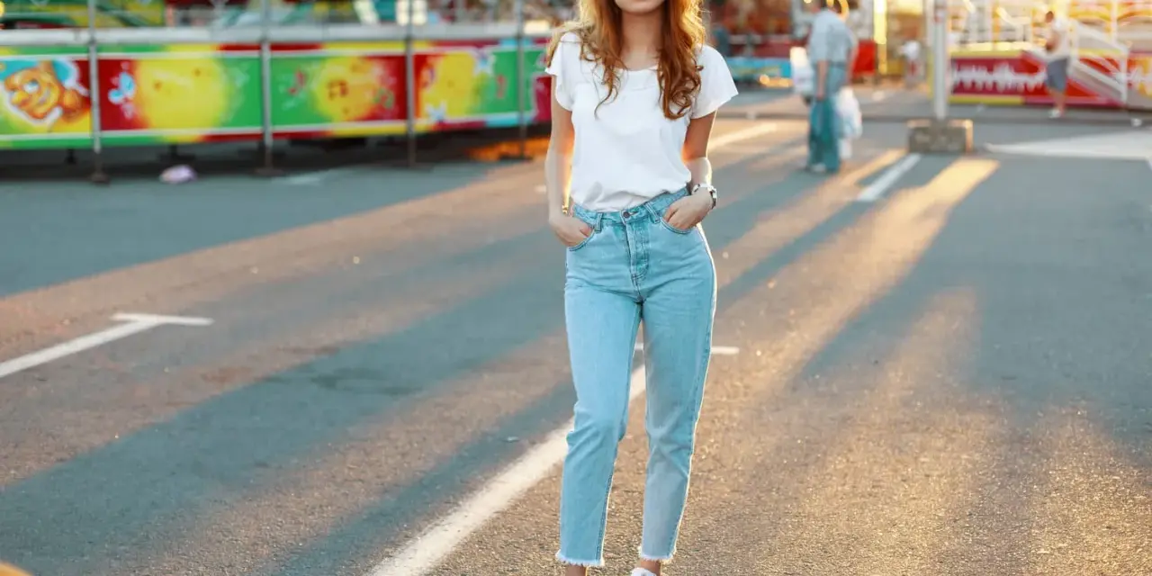 Une jeune femme porte un jean mom et des baskets blanches, un look parfait pour une journée à la fête foraine.