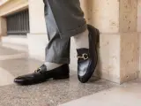 Un homme porte un pantalon gris retroussé et une chaussette mocassin noire avec une boucle dorée.