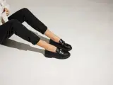 Une tenue décontractée avec un jean noir et une veste claire, rehaussée par une élégante tenue avec mocassin femme orné d'une chaîne dorée.
