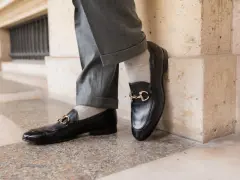 Un homme porte un pantalon gris retroussé et une chaussette mocassin noire avec une boucle dorée.