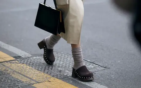 Une femme marche dans la rue, portant un sac noir et un élégant sabot femme marron clouté avec des chaussettes grises.