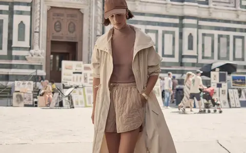 Une femme porte un ensemble athleisure chic : short matelassé, haut col roulé, veste longue et casquette. Elle se promène devant une cathédrale.