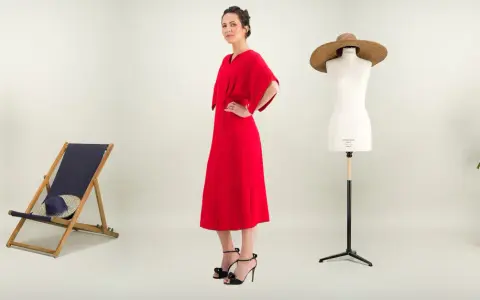 Une femme pose dans une robe rouge éclatante. À ses côtés, une chaise longue, un mannequin de couture et des plantes. Une robe casual, c'est quoi ?