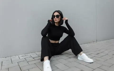 Une femme en tenue noire, crop top et pantalon large, assise sur des pavés. Idée de comment porter un pantalon large avec des baskets blanches.