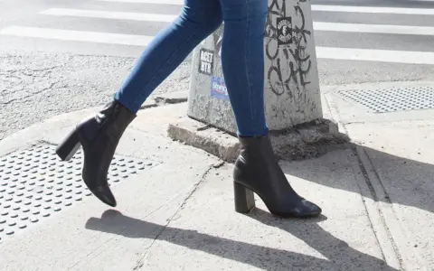 Une femme marche dans la rue avec un jean slim et des bottines noires à talons.