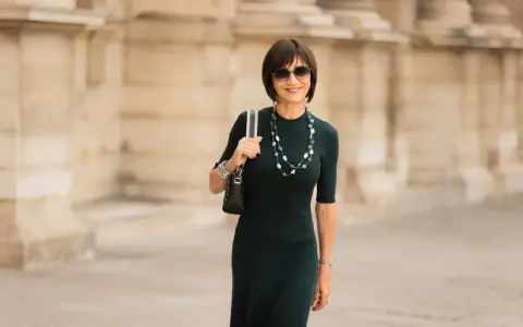 Une femme élégante porte une robe midi vert foncé, un collier de perles et des lunettes de soleil. La robe midi définition est une longueur polyvalente.