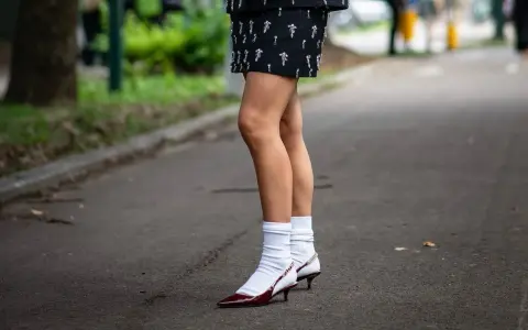 Jambes portant une jupe ornée et des escarpins bordeaux avec une chaussette par dessus chaussure blanche.