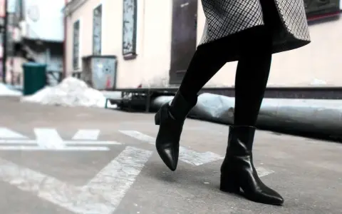Une femme porte une tenue avec des chelsea boots femme noires, un manteau à carreaux et des collants.