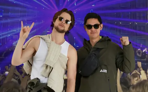 Deux amis profitent d'un concert, l'un fait un signe rock'n'roll, l'autre un poing levé. Leur tenue festival pluie est parfaite pour l'ambiance.